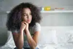 Lonely young latina woman sitting on bed with sad expression on her face.
