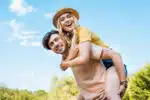view of a happy couple outside, man carrying woman piggyback