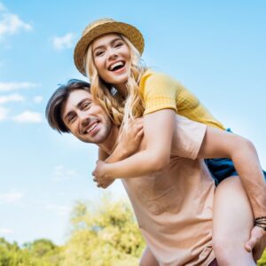 view of a happy couple outside, man carrying woman piggyback