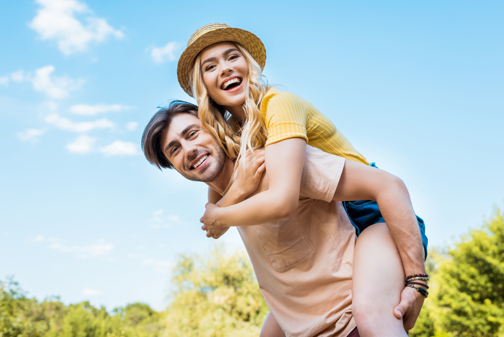 view of a happy couple outside, man carrying woman piggyback