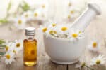 Essential oil and camomile flowers in mortar.