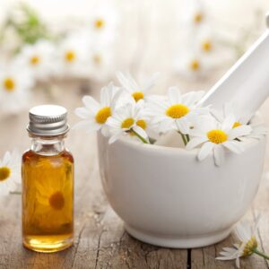 Essential oil and camomile flowers in mortar.