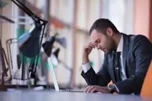 Business man at the office looking stressed at his desk in front of a laptop.