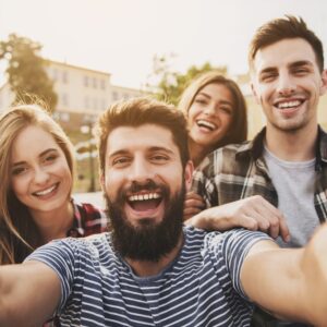 Four young happy people posing together for a selfie outside.