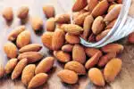 Raw almonds spilling out of a small glass bowl.