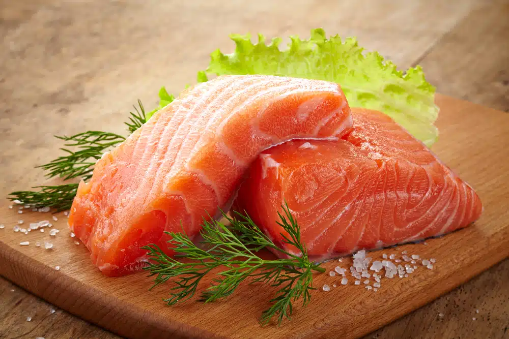 Two raw slices of salmon fish sitting on a small cutting board.