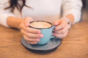 Close up of coffee mug on a table with a woman's hands wrapped around them.