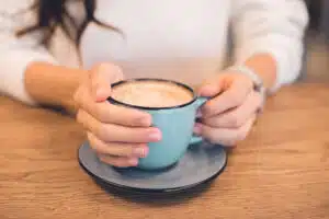 Close up of coffee mug on a table with a woman's hands wrapped around them.