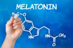 Hand with pen drawing the chemical formula of melatonin.
